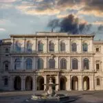 Historic building with fountain under dramatic sky.