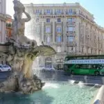 Triton Fountain in sunny city square with tour bus.